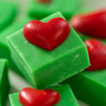 Homemade chocolate green fudge with red hearts square pieces on a white plate.