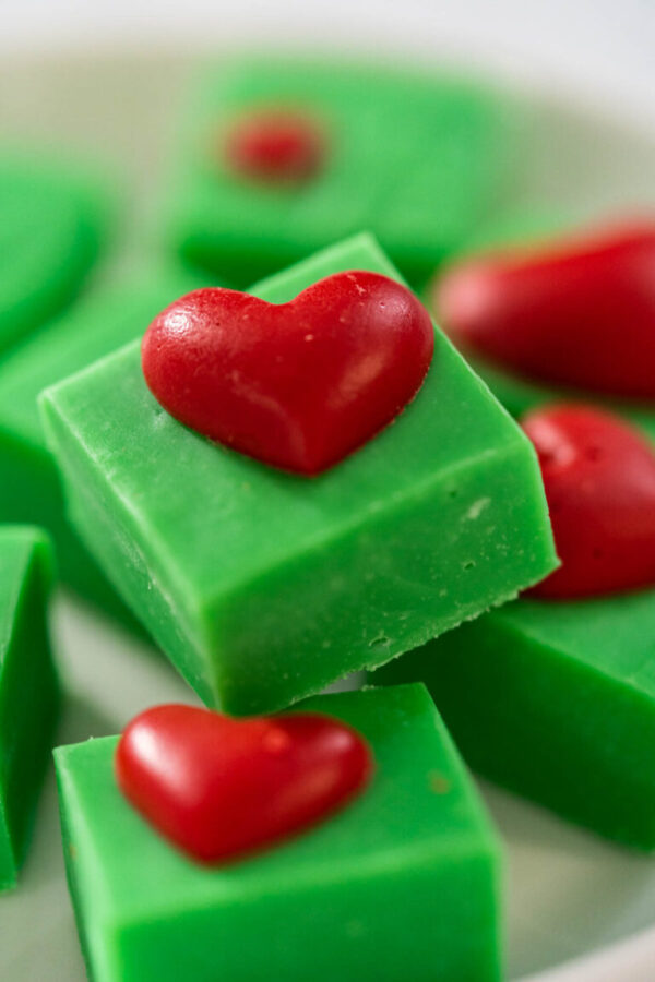 Homemade chocolate green fudge with red hearts square pieces on a white plate.