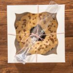 Flat lay. Carefully placing the gingerbread bundt cake, adorned with salted caramel frosting and gingerbread sprinkles, into a white paper bundt cake box with a clear window for gifting.