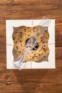 Flat lay. Carefully placing the gingerbread bundt cake, adorned with salted caramel frosting and gingerbread sprinkles, into a white paper bundt cake box with a clear window for gifting.