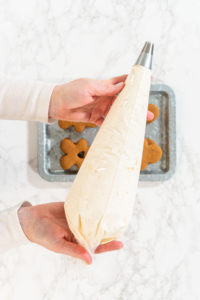 Creating Gingerbread Cookie Sandwiches with Buttercream Filling - Arina Photography Flat lay. Gingerbread cookies await their second halves on a marble surface, each meticulously piped with buttercream to craft delightful sandwich treats. The precision of the piping adds a festive touch.