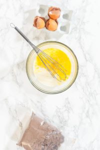 Baking Chocolate Cupcakes with Decadent Chocolate Frosting - Arina Photography Whisk blending milk and beaten eggs in a clear bowl for cupcake batter.