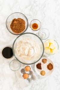 Classic Gingerbread Cookie Dough for Holiday Baking - Arina Photography Overhead view of the ingredients arranged for making Classic Gingerbread Cookie Dough, showcasing individual portions of flour, brown sugar, molasses, spices, and other essentials on a light marble background. The neatly organized display highlights the rich, warm tones of the spices and the dark molasses, creating a festive, holiday baking aesthetic.