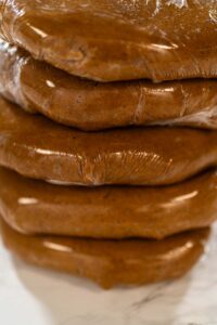 Classic Gingerbread Cookie Dough for Holiday Baking - Arina Photography Discs of Classic Gingerbread Cookie Dough are stacked and wrapped in plastic, ready for chilling before being rolled out. Chilling helps the dough hold its shape, making it easier to cut into festive cookies.