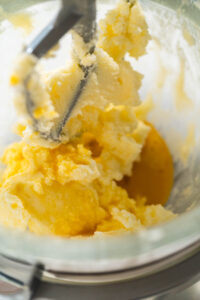 View of the mixer creaming butter, sugar, and an egg for Classic Sugar Cookie Dough. The ingredients are partially blended, highlighting the fluffy, creamy texture that forms the foundation of the cookie dough.