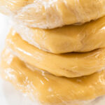Tight shot of plastic-wrapped cookie dough, showing firm texture before rolling and cutting into shapes.
