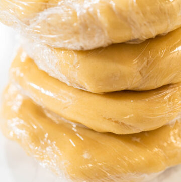 Tight shot of plastic-wrapped cookie dough, showing firm texture before rolling and cutting into shapes.