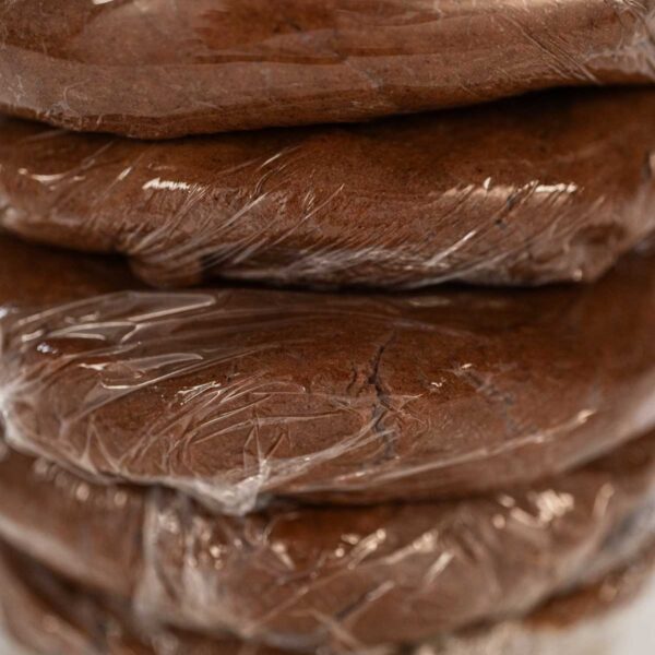 Chocolate Ginger Sugar Cookie Dough for Baking - Arina Photography Stacked discs of Chocolate Ginger Sugar Cookie Dough wrapped in plastic, ready to chill, showing a smooth and uniform dough texture.