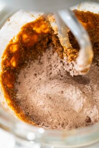Chocolate Gingerbread Cookie Dough for Holiday Baking - Arina Photography Adding dry ingredients, including flour and cocoa powder, to the wet ingredients in the mixer for Chocolate Gingerbread Cookie Dough. This step begins the process of forming a soft and flavorful dough.