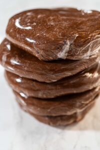 Chocolate Gingerbread Cookie Dough for Holiday Baking - Arina Photography Multiple discs of Chocolate Gingerbread Cookie Dough wrapped in plastic wrap, stacked and ready to chill. These dough discs make it convenient to shape cookies for holiday baking.