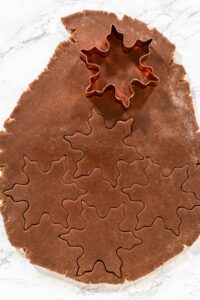A close-up of snowflake-shaped cookie cutters pressed into Chocolate Ginger Sugar Cookie dough, capturing the intricate details of the shapes.