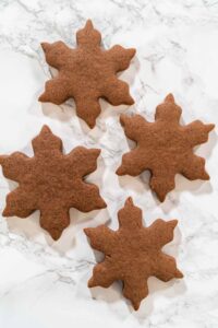 Grouped arrangement of three Chocolate Ginger Sugar Cookies in snowflake shapes on a marble surface, showcasing their uniform design and festive appeal.