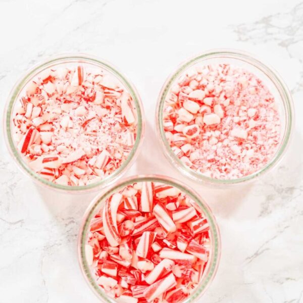 Preparing Crushed Candy Canes for Baking Projects - Arina Photography Three glass bowls filled with crushed candy canes in varying sizes, displayed on a white marble surface.