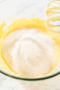 835-05118 - Arina Photography Sifted dry ingredients including flour, baking powder, salt, and cream of tartar piled on top of the lemon cookie batter in a glass mixing bowl, ready to be mixed into dough.