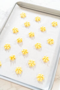 835-05125 - Arina Photography Freshly pressed lemon spritz cookies arranged on a parchment-lined baking sheet, ready to be baked.