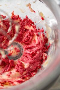 835-05174 - Arina Photography Partially mixed cranberry buttercream frosting in a glass mixing bowl, showing swirls of butter and cranberry puree not yet fully blended.
