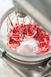 835-05179 - Arina Photography Glass mixing bowl with cranberry buttercream mixture and a mound of powdered sugar on top, ready to be blended with a whisk attachment.