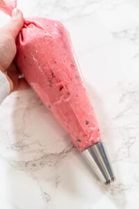 835-05207 - Arina Photography Piping bag filled with cranberry buttercream, fitted with a metal star tip, ready for decorating.