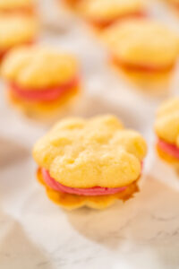 835-05284 - Arina Photography Lemon spritz sandwich cookie filled with cranberry buttercream, displayed on parchment paper.