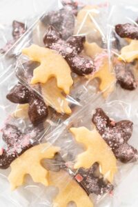 Making Chocolate Dipped Peppermint Sugar Cookies - Arina Photography Chocolate dipped peppermint cut-out sugar cookies shaped like moose, packaged in clear treat bags for holiday gifting. Half of each cookie is coated in dark chocolate and sprinkled with crushed candy cane pieces.