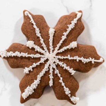 Close-up of a chocolate snowflake cookie decorated with white royal icing and sparkling sugar crystals, ideal for winter-themed holiday treats and Christmas dessert tables.