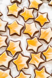 Perfectly Icing Star Cookies with Royal Icing - Arina Photography Overhead view of iced star cookies painted with edible gold luster dust, arranged on a marble surface—perfect for festive holiday cookie boxes or dessert tables.