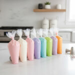 Colorful piping bags filled with pastel royal icing lined up on a white kitchen counter for the blog post How to Make Royal Icing for Decorating Sugar Cookies.